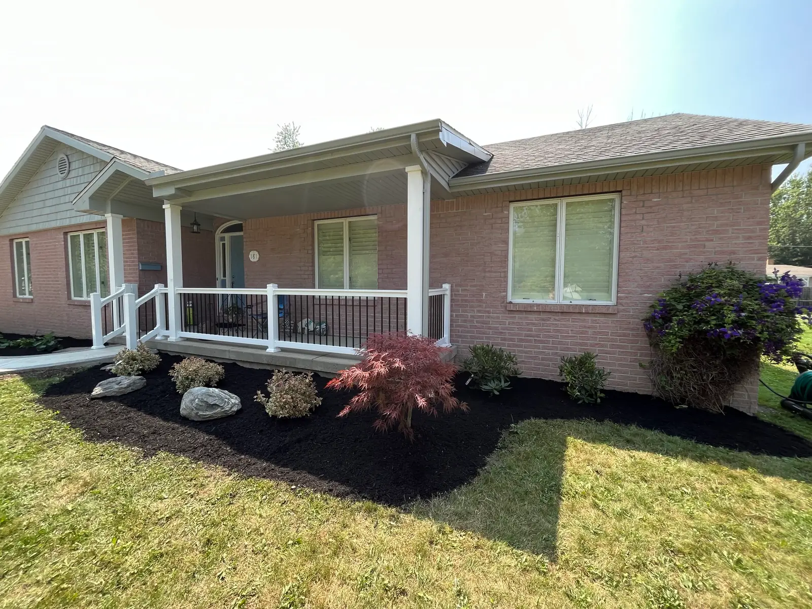 Freshly landscaped porch with ornamental plants, boulders, and black mulch